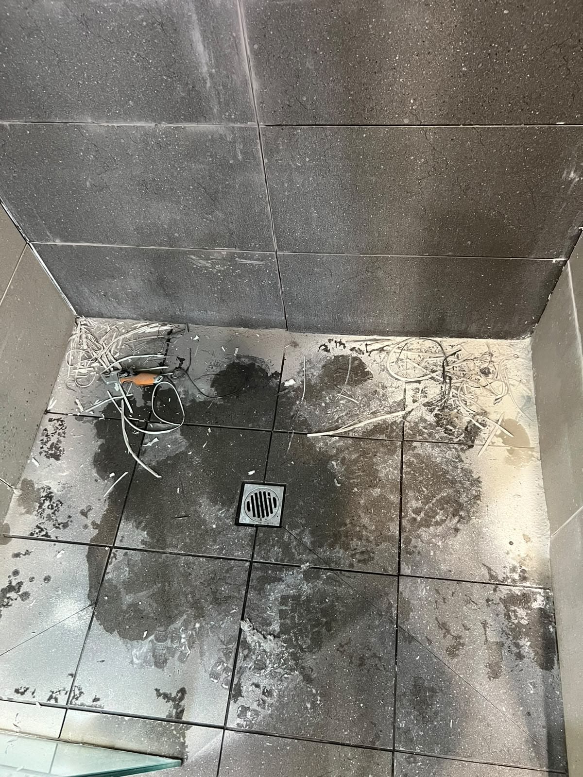 Dark speckled shower floor with old grout raked out around square drain — Melbourne