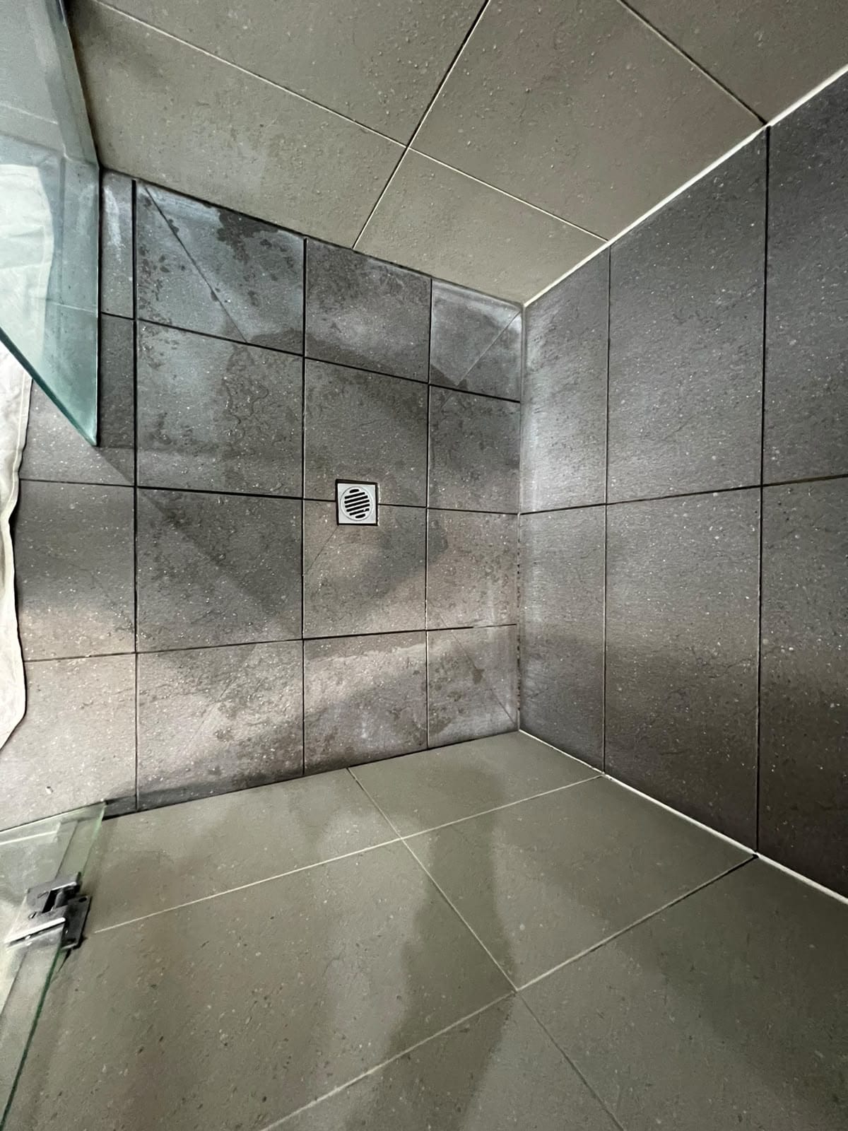 Completed dark speckled shower floor regrouting with crisp white joints — Melbourne