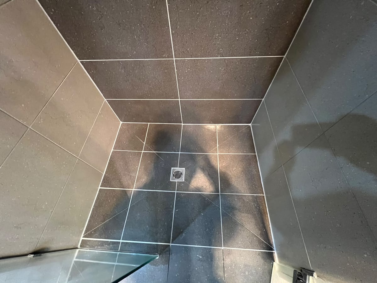 Dark speckled shower floor finished with crisp new grout lines around square drain — Melbourne