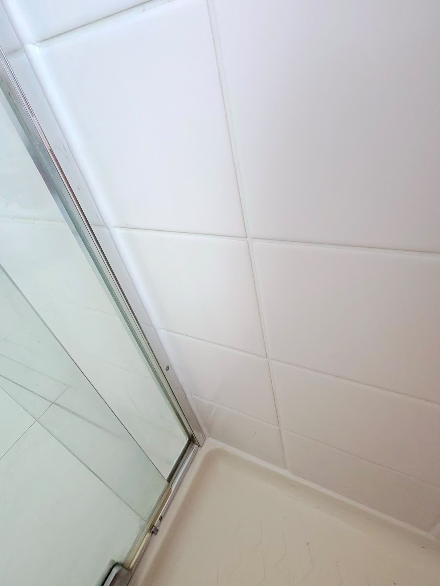 Shower screen corner junction after full grout restoration and fresh white silicone — Melbourne