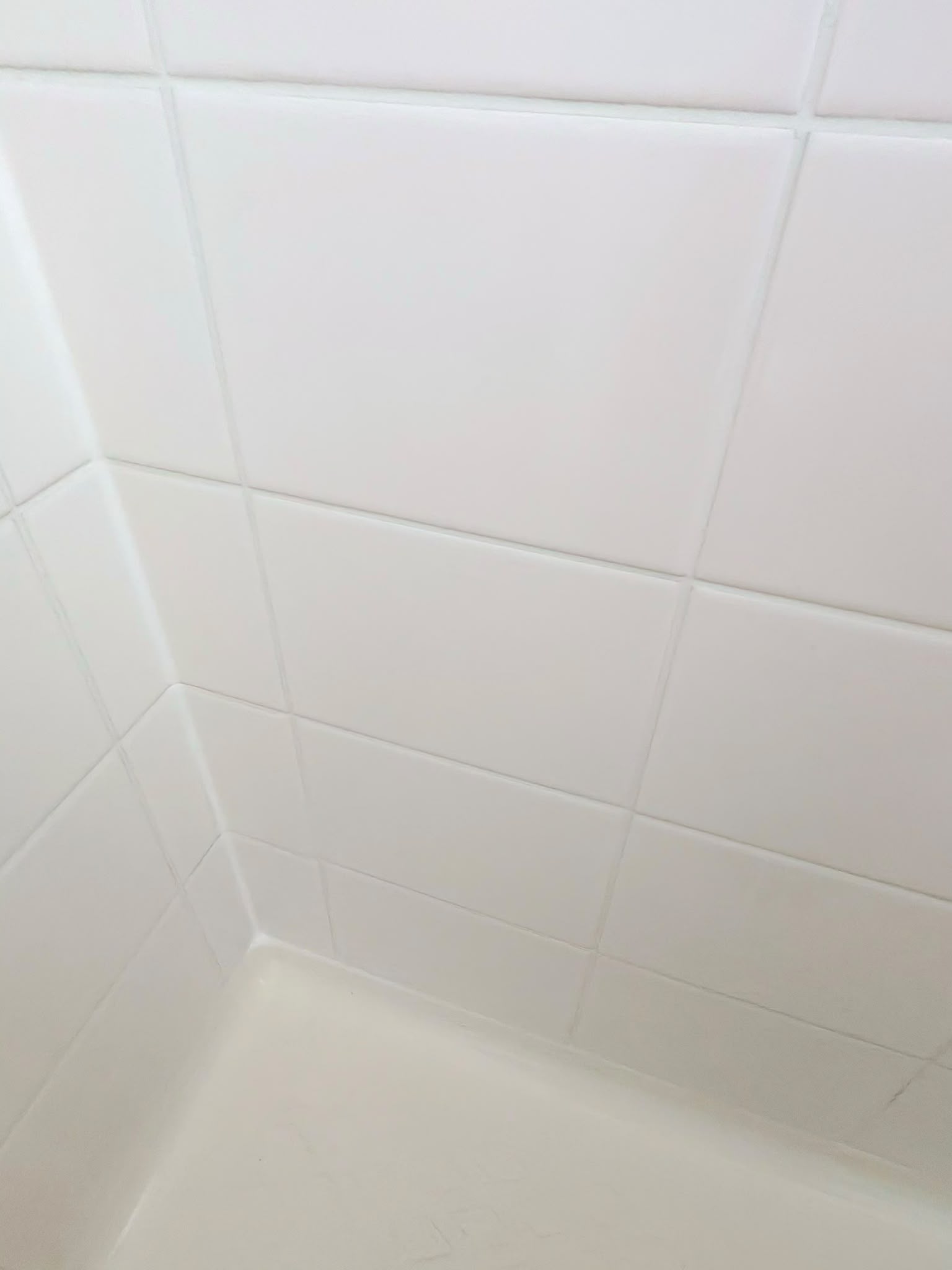 Clean white shower wall tiles and sealed shower base perimeter after regrouting — Melbourne