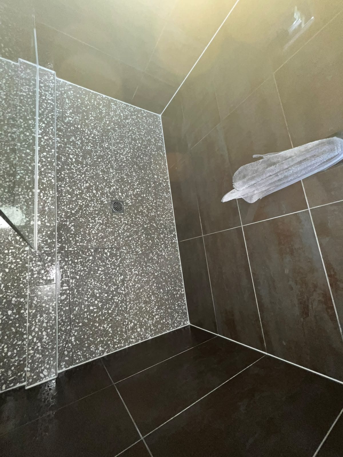 Completed terrazzo-speckled shower floor and brown wall tiles with fresh white grout — Melbourne
