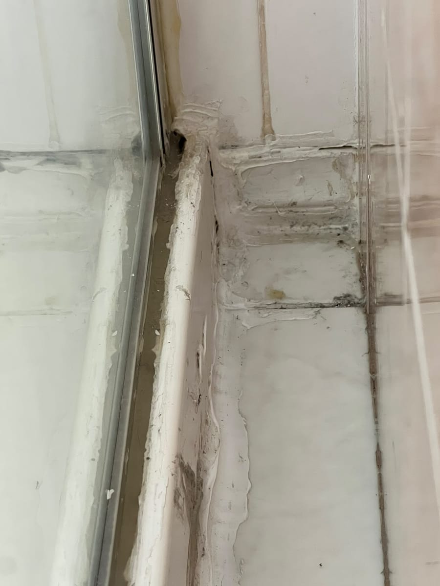 Tradesperson removing split and mouldy shower silicone with precision tool