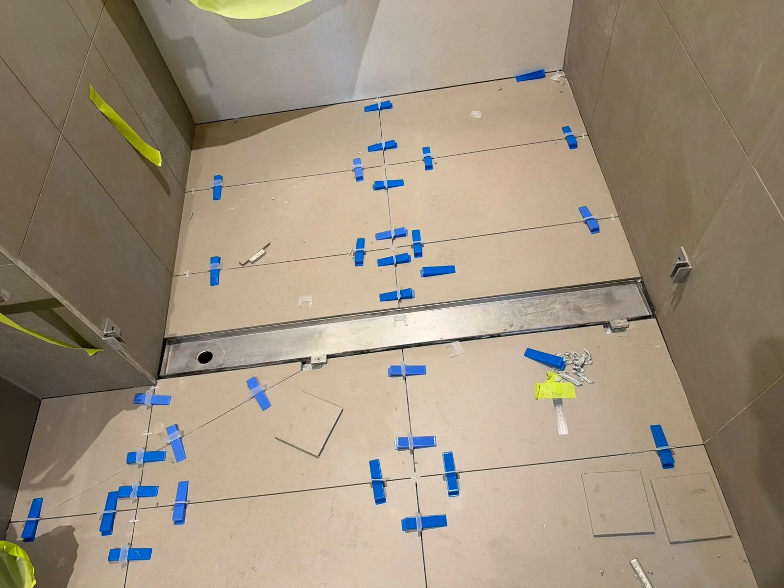 Shower floor porcelain tiles being levelled around stainless steel linear drain — Melbourne